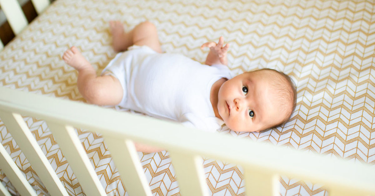 A baby lying on their back in a crib.