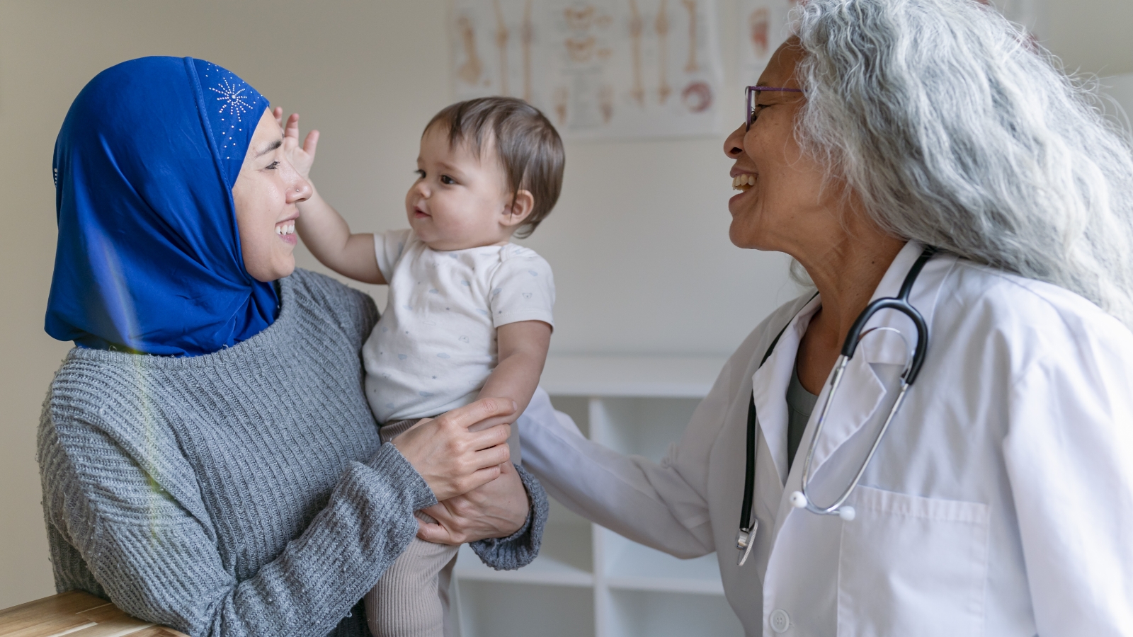 A caregiver holds a baby in their arms while a healthcare provider looks on.