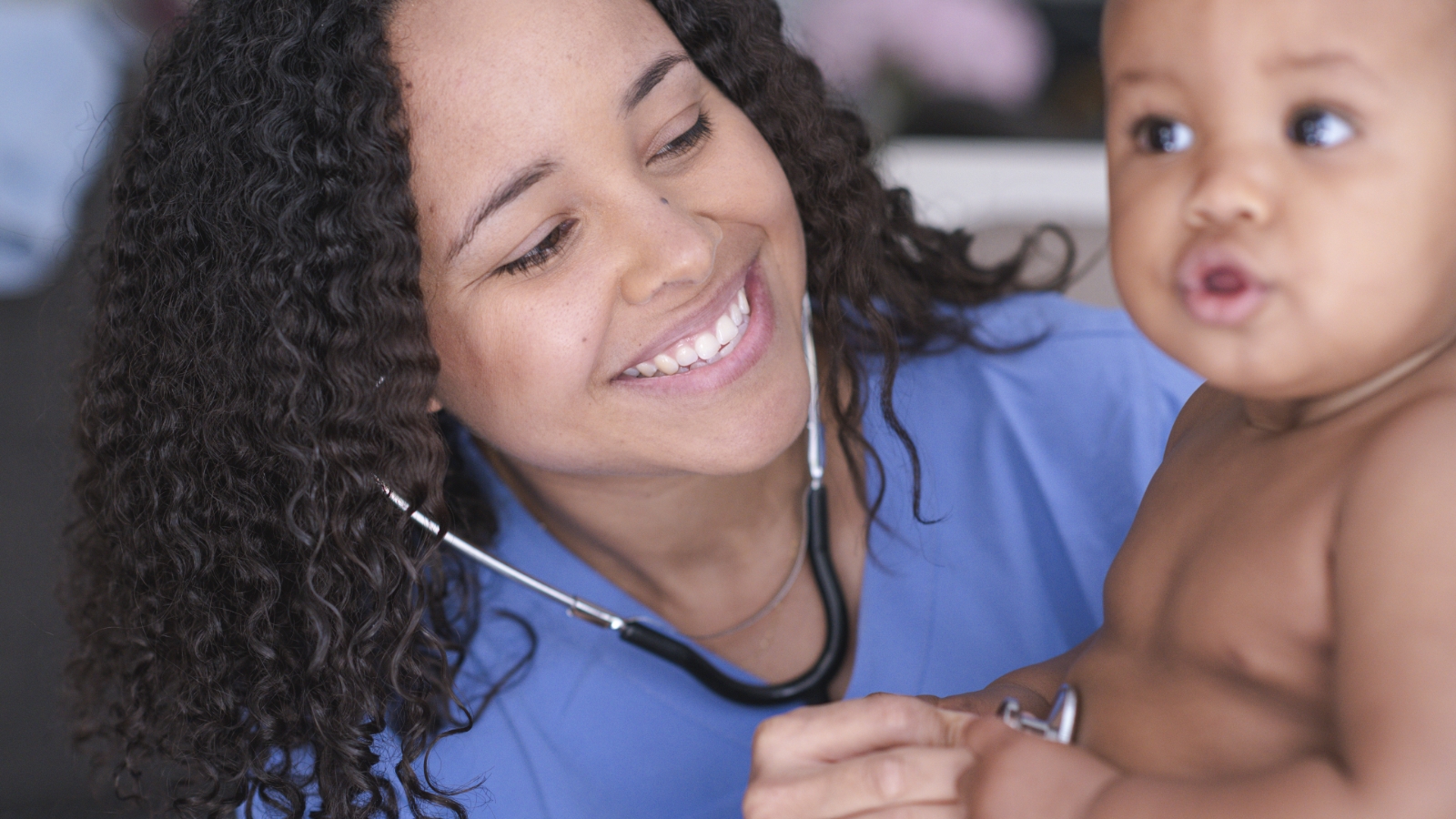 A nurse (left) is smiling at a baby (right)