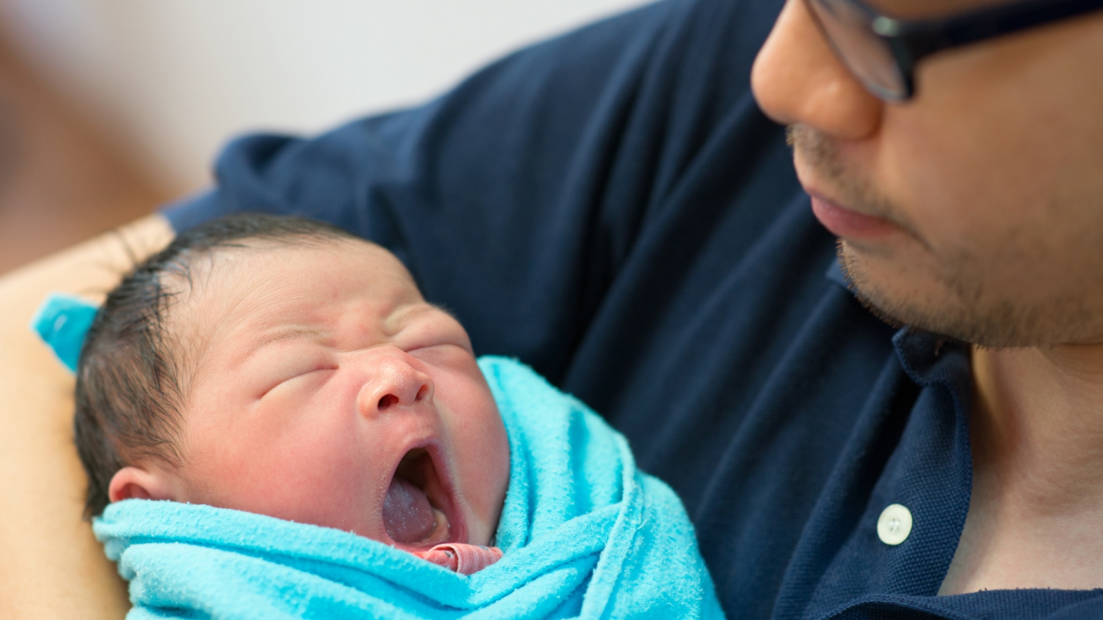 A baby yawns while swaddled in a caregiver's arms.