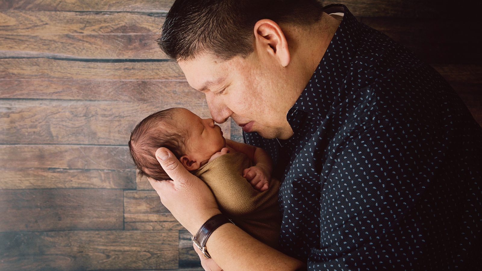  A father is holding a baby in his arms, pulling the baby towards his face