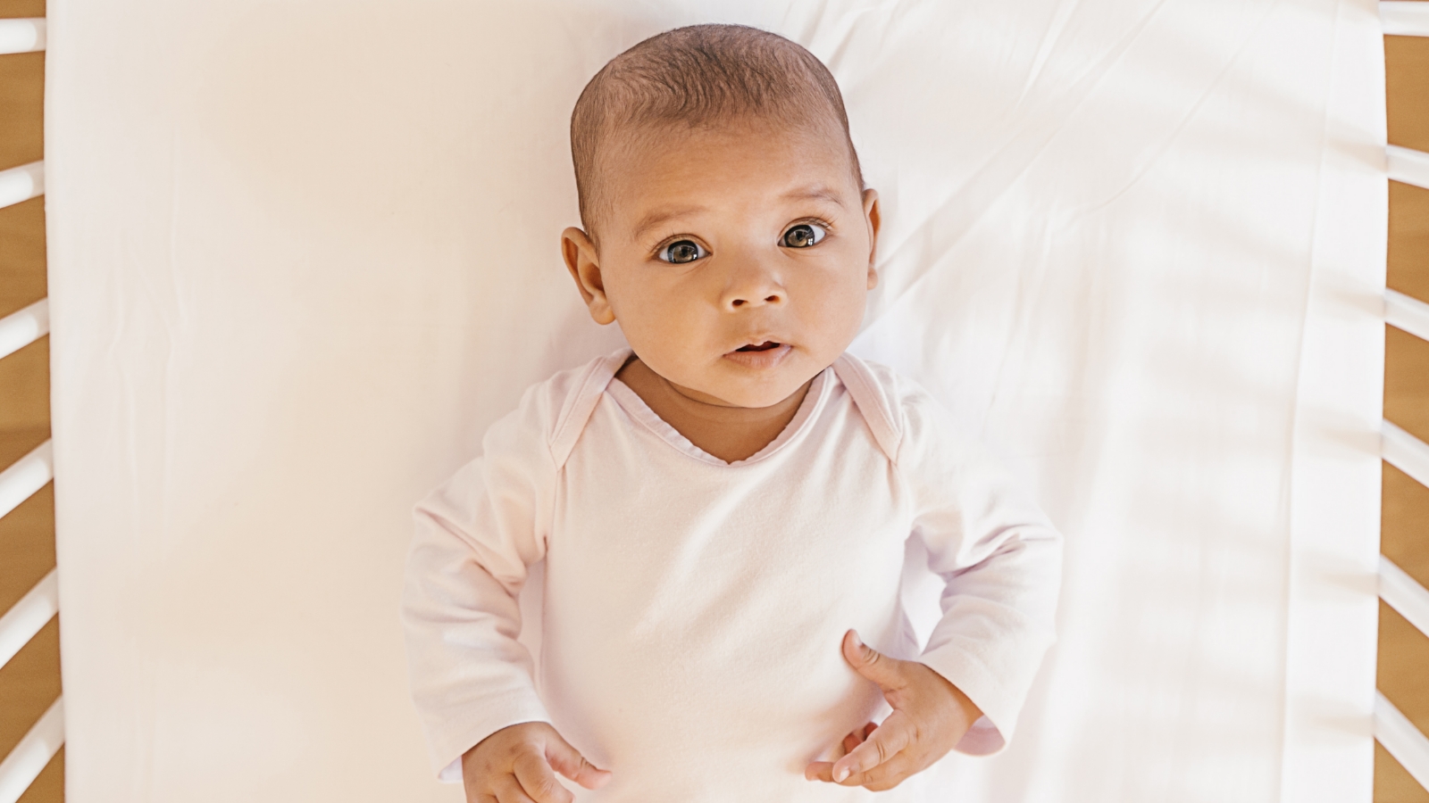 An overhead view of a baby lying on their back in an empty crib.