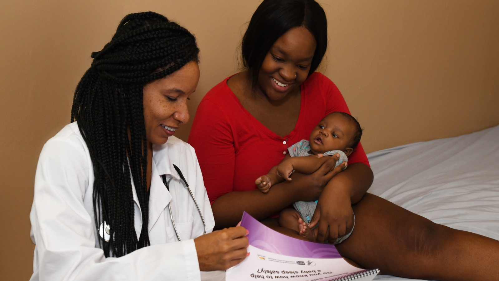 A healthcare provider (left) going over materials with a mother (right) who is holding a baby