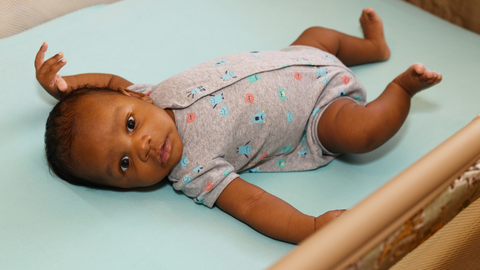 A baby lies on its back in an empty crib.