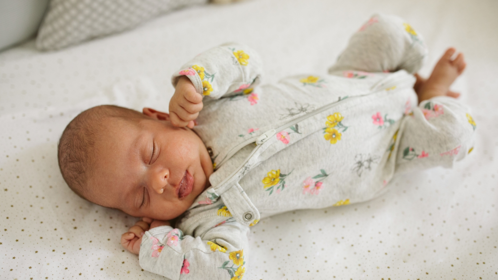 A baby lies on their back, with hands up near the face. The sleep area is free of toys, bedding, and other items.