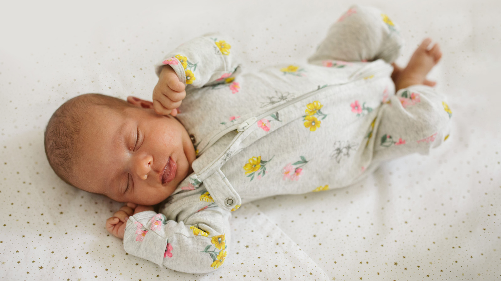 A baby lies on their back, with hands up near the face. The sleep area is free of toys, bedding, and other items.