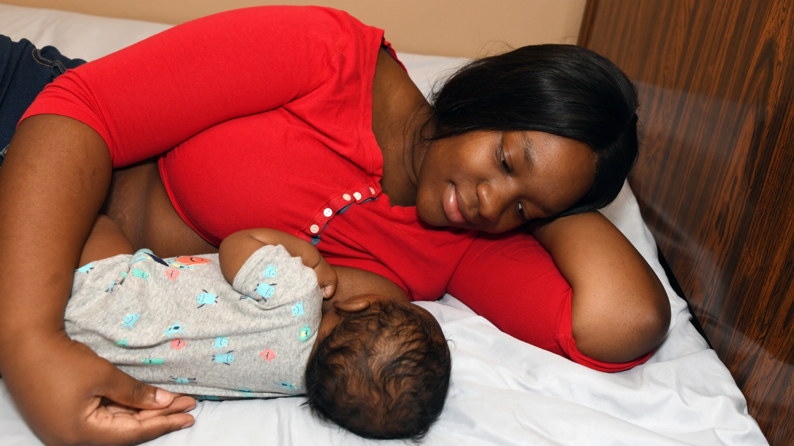 A mother breastfeeds a baby as they lie in bed.
