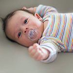 A baby lies on his back with a pacifier in his mouth.